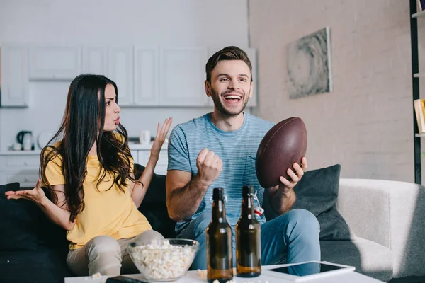 愤怒的年轻女子大喊大叫的丈夫 而他看美国足球在电视上在家里 — 图库照片