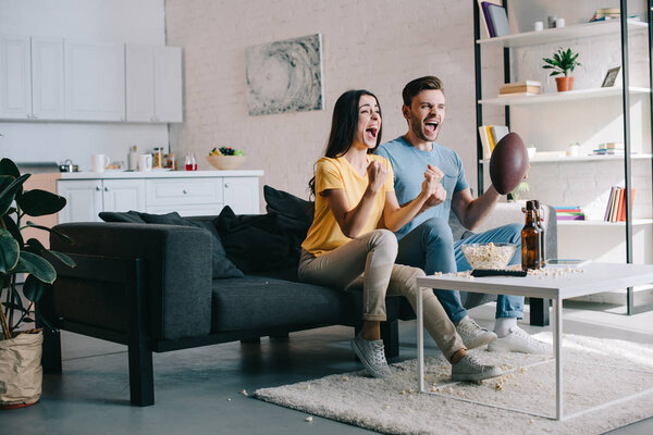 expressive young couple cheering for american football game at home