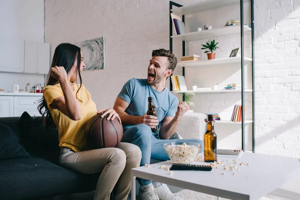 情绪激动的年轻夫妇与啤酒欢呼篮球比赛在家里 — 图库照片