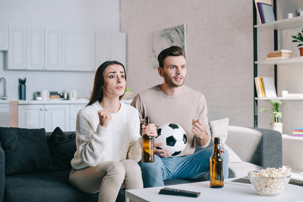 excited young couple watching football game on couch at home