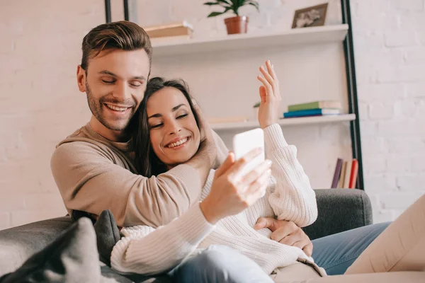 Sonriente Pareja Joven Utilizando Teléfono Inteligente Juntos Sofá Casa — Foto de Stock