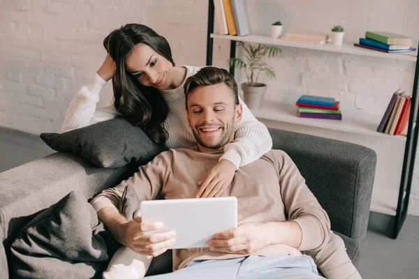 Sorridente Giovane Coppia Utilizzando Tablet Insieme Sul Divano Casa — Foto Stock