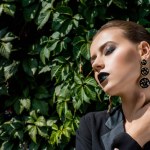 Beautiful young woman with sunbeams on face and green leaves at background