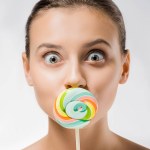 Mujer atractiva joven escondiendo la boca detrás de piruleta de colores