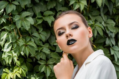 arka plan, yeşil yaprakları ile yüz dokunmadan Beyaz ceketli şık genç kadın