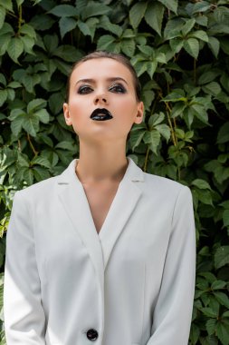 arka plan, yeşil yaprakları ile Beyaz ceketli şık genç kadın