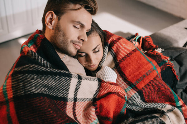 high angle view of beautiful young couple relaxing on couch and covering with plaid
