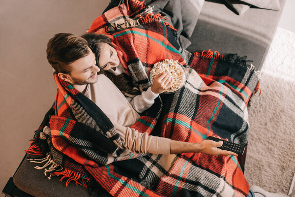 высокий угол зрения красивой молодой пары смотреть телевизор с попкорном на диване и покрытия клетчатой

