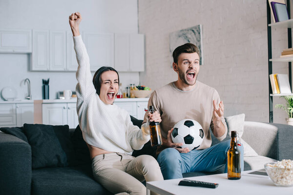 expressive young couple watching football game at home and cheering