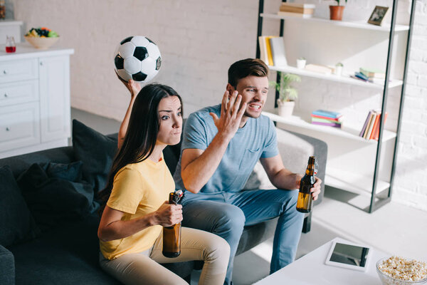 expressive mad young couple watching football game at home