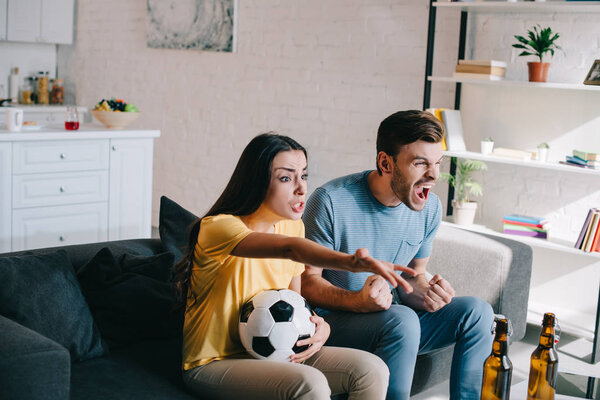 expressive shouting young couple watching football game at home