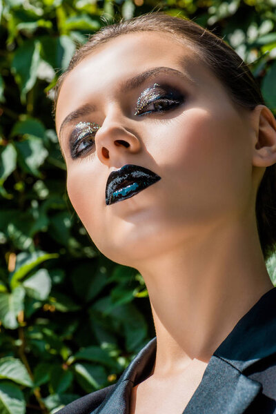 young woman with shiny makeup looking at camera at green background 