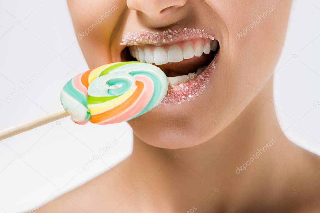 close up of young woman with sugar on lips biting colored lollipop