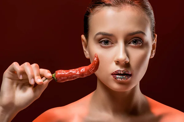年轻的迷人的女人与闪亮的嘴唇和红色辣椒在勃艮第背景 — 免费的图库照片