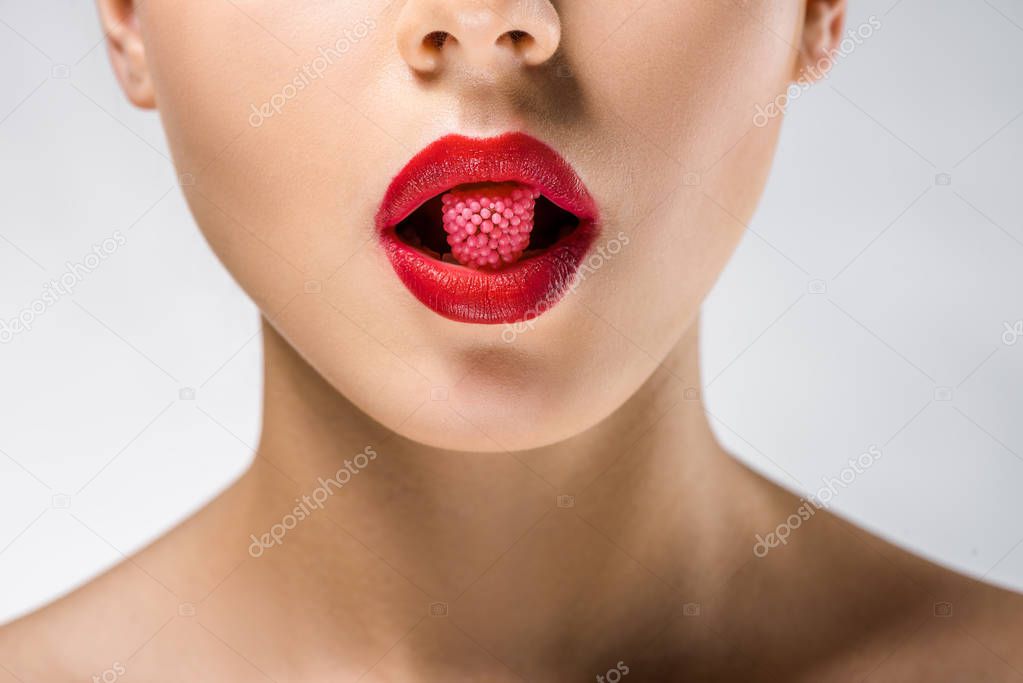 close up of young woman with red lips holding red candy in mouth