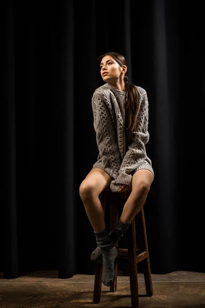 ウールのセーターと黒の背景のバースツールの上に座って靴下で美しい女性 — ストック写真