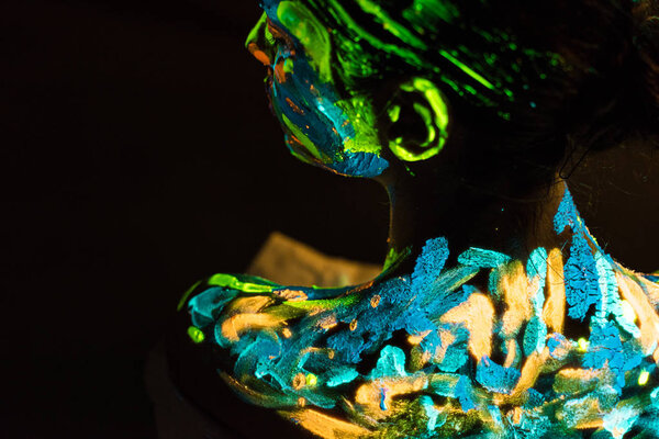 back view of model with colorful neon paints on body on black background