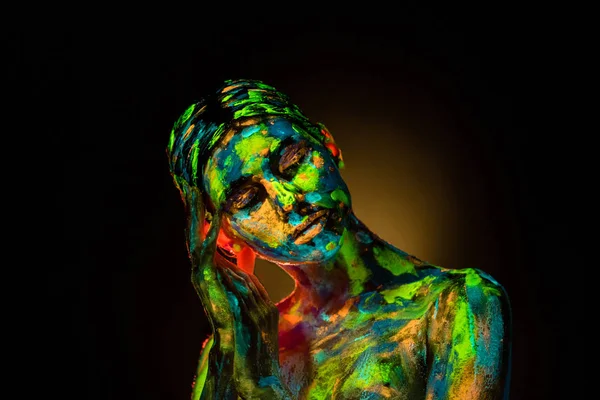 portrait of beautiful woman with colorful ultraviolet paints on body on black backdrop
