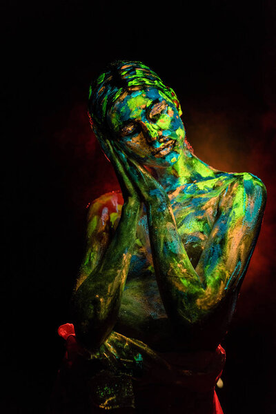 portrait of beautiful woman with colorful ultraviolet paints on body on black backdrop