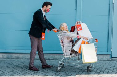Alışveriş torbaları ve alışveriş sepeti ile eğleniyor mavi duvar Satılık Etiketler ile mutlu çift