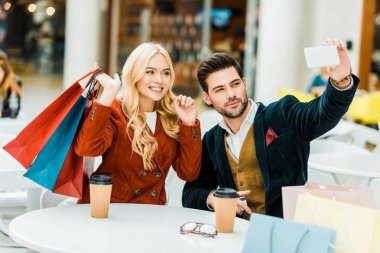 Alışveriş torbaları ve selfie alışveriş merkezi smartphone taking gitmek için kahve ile şık çift