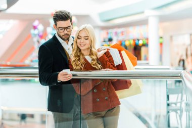alışveriş alışveriş merkezinde smartphone kullanarak torbaları ile şık genç çift