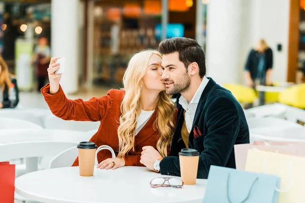 Beautiful Girl Kissing Boyfriend Taking Selfie Smartphone Shopping Mall — Free Stock Photo