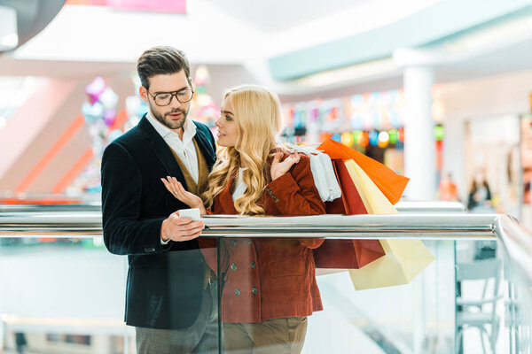 beautiful stylish couple with shopping bags using smartphone in shopping center