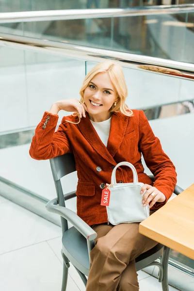 Beautiful Blonde Girl Sitting Mall Holding Bag Sale Tag — Free Stock Photo