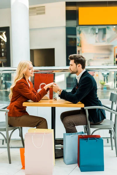 Piękna Para Trzymając Się Ręce Siedzi Torby Zakupy Kawiarni Centrum — Darmowe zdjęcie stockowe