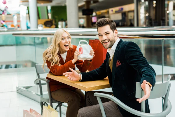 Excited Female Shopaholic Showing Bag Sale Tag Laughing Boyfriend — Free Stock Photo