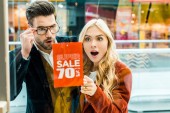 schönes aufgeregtes Paar von Shopaholics, die Superverkauf mit 70 Prozent Rabatt im Einkaufszentrum betrachten