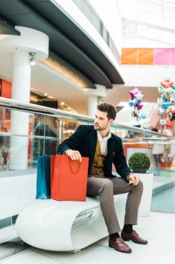 kredi kartı tutan ve elinde çanta alışveriş merkezinde oturan moda adam