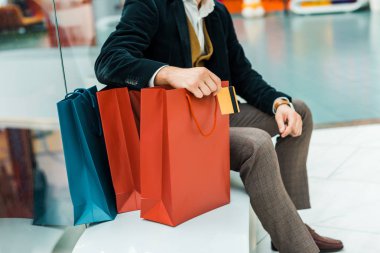 kredi kartı tutan ve çanta alışveriş merkezi ile oturan adam görünümünü kırpılmış