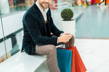 Alışveriş merkezinde çanta ile akıllı telefon kullanan şık adam görünümünü kırpılmış