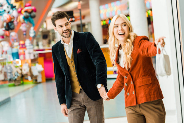 beautiful excited girl showing something to boyfriend in shopping mall