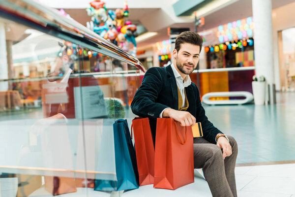 stylish elegant man sitting in shopping mall with bags