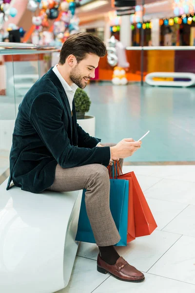 Alışveriş merkezinde çanta ile akıllı telefon kullanan şık adam