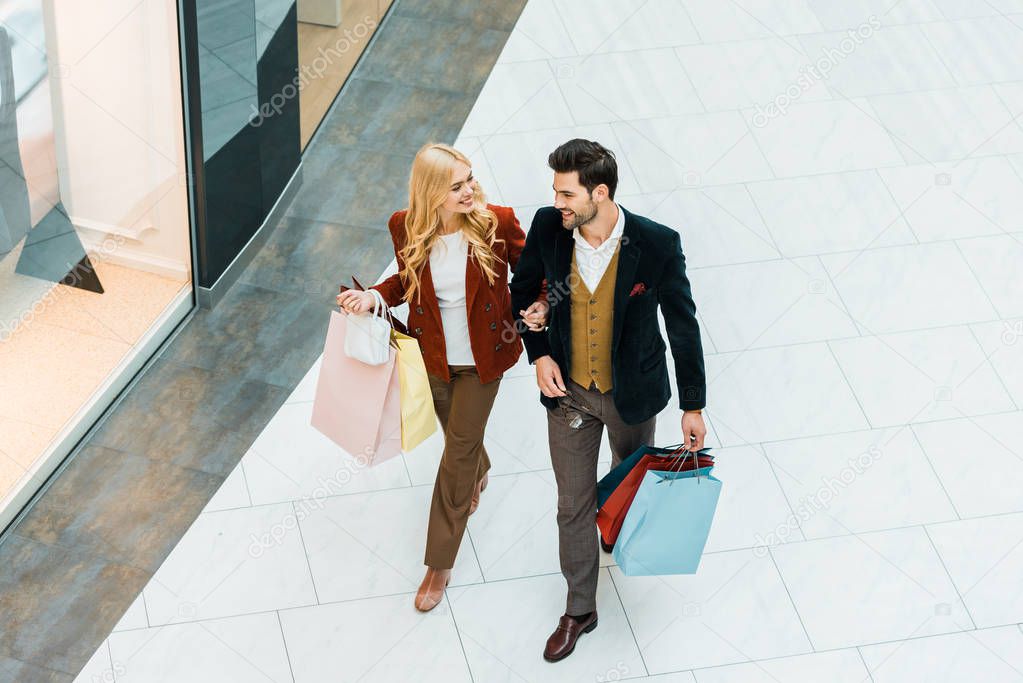 overhead view of young couple of shopaholics with bags walking in shopping mall
