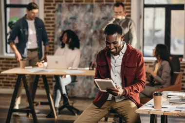 Tablet arkasında çalışma çatı office meslektaşları ile tutarak gülümseyen Afro-Amerikan rahat iş adamı