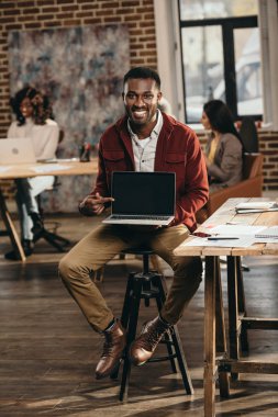 Afro-Amerikan rahat işadamı laptop ile boş bir ekran ve arkasında çalışma çatı office meslektaşları tutan