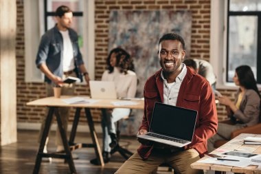 Afro-Amerikan rahat işadamı laptop ile boş bir ekran ve arkasında çalışma çatı office meslektaşları tutan