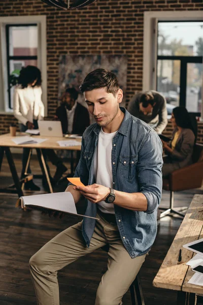 Joven Sosteniendo Diario Mirando Nota Oficina Loft Moderna Con Colegas — Foto de Stock