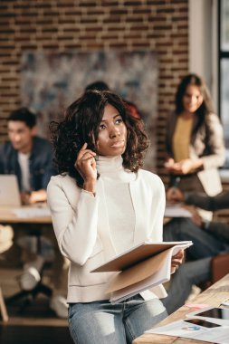 oturma ve smartphone loft Office arkasında çalışma arkadaşları ile konuşurken Afro-Amerikan rahat iş kadını