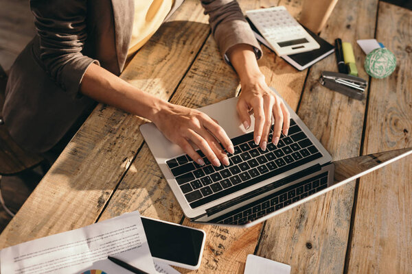 cropped view of female hands typing on laptop at desk with office supplies