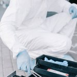 Criminólogo masculino en traje de protección y guantes de látex tomando pinzas de bolsa de herramientas de investigación