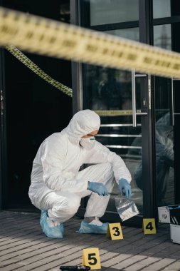 male criminologist in protective suit and latex gloves packing evidence with wizzles at crime scene clipart