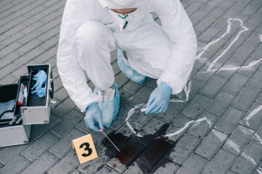 male criminologist in protective suit and latex gloves taking a blood sample at crime scene clipart