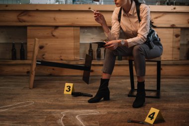 cropped view of smoking female detective sitting at crime scene with evidence markers and dead body outline clipart