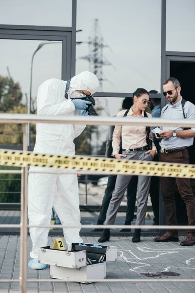 Criminologist making photo of crime scene on camera with two detectives behind him
